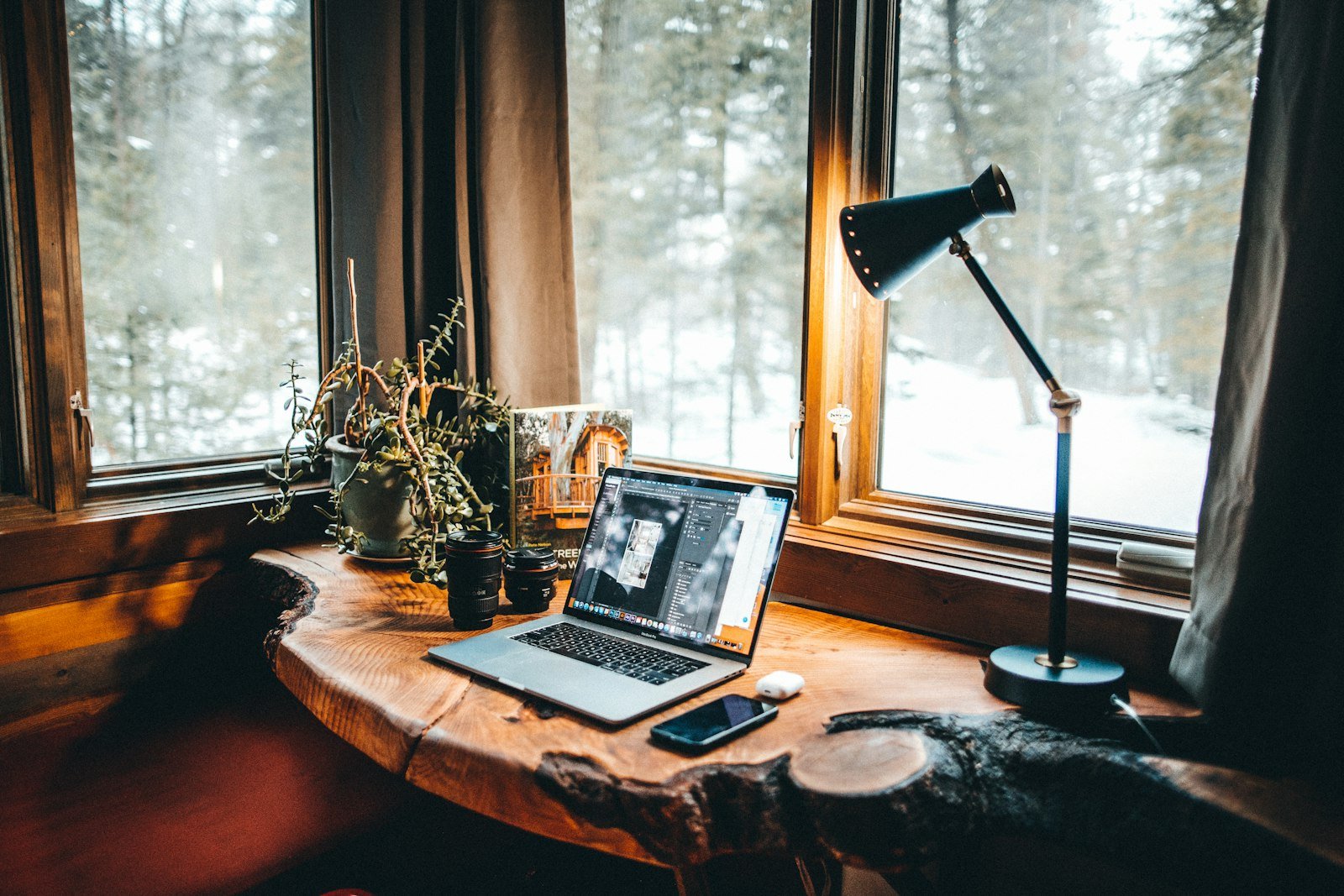 Bureau en bois chaleureux avec lampe, plantes et ordinateur portable près d’une fenêtre